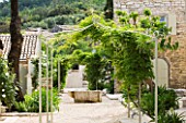 THE ROU ESTATE  CORFU: THE MAIN PATHWAY THROUGH THE VILLAGE WITH PERGOLA COVERED IN WISTERIA AND WELL