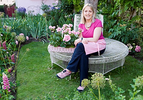 PAULA_PRYKES_HOUSE__SUFFOLK_PAULA_RELAXES_ON_WHITE_METAL_TREE_SEAT_NEXT_TO_A_TRAY_OF_SCENTED_PELARGO