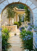 CORFU  GREECE: DESIGNER: DOMINIC SKINNER - MEDITTERANEAN STYLE GARDEN WITH STONE ARCH AND AGAPANTHUS