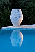 CORFU  GREECE: DESIGNER: DOMINIC SKINNER - MEDITTERANEAN STYLE GARDEN  - VIEW TO WHITE TERRACOTTA CONTAINER REFLECTED IN BLUE WATER OF SWIMMING POOL