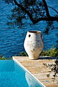CORFU  GREECE: DESIGNER: DOMINIC SKINNER - MEDITTERANEAN STYLE GARDEN  - VIEW TO WHITE TERRACOTTA CONTAINER REFLECTED IN BLUE WATER OF SWIMMING POOL WITH SEA BEYOND
