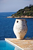 CORFU  GREECE: DESIGNER: DOMINIC SKINNER - MEDITTERANEAN STYLE GARDEN  - VIEW TO WHITE TERRACOTTA CONTAINER REFLECTED IN BLUE WATER OF SWIMMING POOL WITH SEA BEYOND
