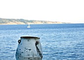 CORFU  GREECE: DESIGNER: DOMINIC SKINNER - MEDITTERANEAN STYLE GARDEN  - VIEW TO WHITE TERRACOTTA CONTAINER BESIDE SWIMMING POOL WITH SEA AND SAILING BOAT BEYOND