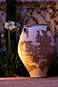 CORFU  GREECE: DESIGNER: DOMINIC SKINNER - MEDITTERANEAN STYLE GARDEN  - BEAUTIFUL TERRACOTTA CONTAINER LIT UP AT NIGHT WITH AGAPANTHUS