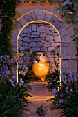 CORFU  GREECE: DESIGNER: DOMINIC SKINNER - MEDITTERANEAN STYLE GARDEN  - VIEW ALONG BRICK PATH TO FOCAL POINT TERRACOTTA CONTAINER  ARCH AND AGAPANTHUS