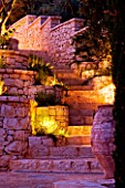 CORFU  GREECE: DESIGNER: DOMINIC SKINNER - MEDITTERANEAN STYLE GARDEN  - BEAUTIFUL STONE STEPS AND WALL WITH TERRACOTTA CONTAINER LIT UP AT NIGHT  LIGHTING