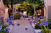 THE ROU ESTATE  CORFU  GREECE: DESIGNER: DOMINIC SKINNER - MEDITTERANEAN STYLE GARDEN - GRAVEL PATH  WELL AND AGAPANTHUS LIT UP AT NIGHT. LIGHTING
