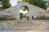 PRIVATE VILLA  CORFU  GREECE. DESIGN BY ALITHEA JOHNS - BRICK STEPS LEADING THROUGH STONE ARCH WITH TWO HUGE TERRACOTTA CONTAINERS