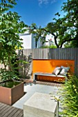 DESIGNERS WYNNIAT- HUSEY CLARKE: MODERN  CONTEMPORARY GARDEN IN BRIGHTON WITH DECKING  ORANGE PANELS ON WALLS  METAL WATER FEATURE  WOODEN BENCH  CUSHIONS  OPHIOPOGON AND ARALIA