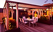DESIGNER: CHARLOTTE ROWE  LONDON: ROOF GARDEN - A PLACE TO SIT - TABLE AND CHAIRS WITH CANDLES LIT UP AT NIGHT WITH WOODEN PERGOLA  SHED  RAISED BEDS AND GLASS SCREEN, DECKS, DECKING, LIGHTS, LIGHTING