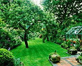 VIEW DOWN GARDEN FROM BACK OF HOUSE WITH WELL-KEPT LAWN & SMALL GREENHOUSE ON LEFT. DESIGNER: MALLEY TERRY