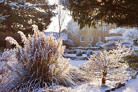 PETTIFERS__OXFORDSHIRE_GARDEN_IN_SNOW_IN_WINTER__VIEW_TOWARDS_THE_HOUSE_WITH_LAWN_AND_BORDER_WITH_AC