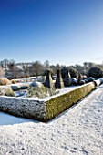 PETTIFERS  OXFORDSHIRE: GARDEN IN SNOW IN WINTER - VIEW TOWARDS THE PARTERRE WITH CLIPPED TOPIARY SHAPES AND THE COUNTRYSIDE BEYOND