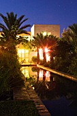 DESIGNERS ERIC OSSART AND ARNAUD MAURIERES  MOROCCO: AL HOSSOUN - COURTYARD SURROUNDING RECTANGULAR POOL AT NIGHT WITH LIGHTS FROM THE BUILDINGS