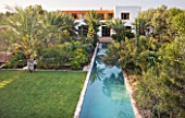 DESIGNERS ERIC OSSART AND ARNAUD MAURIERES  MOROCCO: AL HOSSOUN - THE MAIN POOL/CANAL REFLECTING A SOLANUM  PALM AND AGAVE DESMETTIANA - LAWN