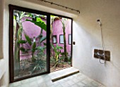DESIGNERS ERIC OSSART AND ARNAUD MAURIERES  MOROCCO: AL HOSSOUN - BATHROOM WITH SHOWER AND VIEW OUT TO GARDEN WITH PURPLE WALL