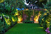 DESIGNER BUTTER WAKEFIELD  LONDON : VIEW FROM THE BACK OF THE HOUSE AT NIGHT WITH THE LAWN AND GREEN BORDERS - TRELLIS AT FAR END - LIGHTING