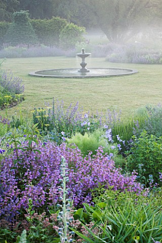 NARBOROUGH_HALL_GARDENS__NORFOLK_DAWN_LIGHT_ON_THE_FOUNTAIN_IN_THE_LAWN_WITH_BLUE_BORDERS_AROUND