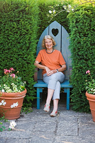 SANDHILL_FARM_HOUSE__HAMPSHIRE__DESIGNER_ROSEMARY_ALEXANDER_SITTING_IN_A_BLUE_WOODEN_SEAT_SET_INTO_A
