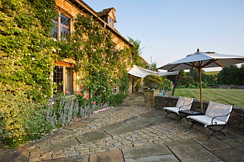 DESIGNER_ALISON_HENRY_PRIVATE_GARDEN_COTSWOLDS__LAWN_STONE_TERRACE__PATIO_WITH_SEATS_AND_CANVAS_SAIL
