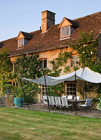 DESIGNER_ALISON_HENRY_PRIVATE_GARDEN_COTSWOLDS__THE_HOUSE_WITH_LAWN_STONE_TERRACE__PATIO_WITH_SEATS_