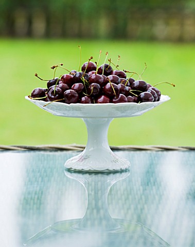 DESIGNER_CLARE_MATTHEWS_CHERRIES_IN_WHITE_BOWL_ON_GLASS_TOPPED_TABLE