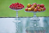 DESIGNER CLARE MATTHEWS: RASPBERRIES AND PLUMS IN GLASS BOWLS ON GLASS TOPPED TABLE