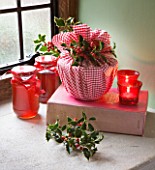 DESIGNER - JACKY HOBBS : CHRISTMAS DECORATION - CANDLES  JAM IN JARS  CHRISTMAS PUDDING WRAPPED IN RED AND WHITE CHECKED CLOTH AND HOLLY BERRIES AND LEAVES  IN WINDOWSILL