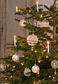DESIGNER: JACKY HOBBS  LONDON: LIVING ROOM AT CHRISTMAS - CHRISTMAS TREE WITH CANDLES  PINE CONES AND BAUBLES