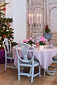 DESIGNER: JACKY HOBBS  LONDON: THE LIVING ROOM AT CHRISTMAS WITH DOOR  WREATH AND CHRISTMAS TREE WITH TABLE SET WITH PINK CYCLAMEN IN CONTAINERS