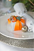 BRUERN COTTAGES  OXFORDSHIRE: CHRISTMAS - PLACE SETTING WITH CRACKER AND PRESENT WRAPPED IN ORANGE RIBBON AND ROSE HIP AND IVY LEAF