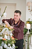BRUERN COTTAGES  OXFORDSHIRE: CHRISTMAS - COLIN BOLAM PUTTING DECORATIONS ONTO THE CHRISTMAS TREE