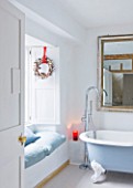 DESIGNER CAROLYN MINTY  GLOUCESTERSHIRE: BATHROOM WITH BATH  MIRROR  WINDOW SEAT AND WREATH. CHRISTMAS