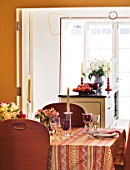 DESIGNER JANE CHURCHILL : THE DINING ROOM WITH KITCHEN BEYOND - YELLOW LINEN WALLS  CUSTOMISED CHAIRS WITH WEBBING AND STUDS ADDED  GLASSES BY IKEA AND WILLIAM YEOWARD
