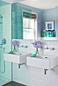 DESIGNER: KALLY ELLIS  LONDON: TWIN WASH BASINS IN BATHROOM WITH GLASS VASES OF LAVENDER SWEET PEAS. CLAUS PORTO SOAP