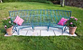 DESIGNER: CLARE MATTHEWS  DEVON - PAVING PROJECT: A PLACE TO SIT: BLUE PAINTED METAL BENCH WITH PINK CUSHIONS AND PATIO ROSES IN TERRACOTTA CONTAINERS