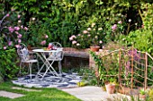 BARBARA KENNINGTON GARDEN  BRIGHTON: PATIO WITH RUSTY METAL RAILINGS  PEBBLE MOSAIC FLOOR AND WHITE TABLE AND CHAIRS WITH CUSHIONS