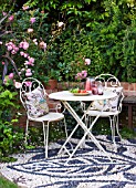 BARBARA KENNINGTON GARDEN  BRIGHTON: PATIO WITH PEBBLE MOSAIC FLOOR  WHITE METAL TABLE AND CHAIRS WITH CUSHIONS