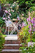 BARBARA KENNINGTON GARDEN  BRIGHTON: STEPS WITH RUSTY METAL RAILINGS LEAD TO PATIO AREA WITH TABLE AND CHAIRS