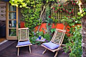KARLA NEWELL GARDEN  BRIGHTON: SMALL TOWN GARDEN WITH ORANGE WALL  DECK CHAIRS WITH BLUE CUSHIONS  FUCHSIA  PYRACANTHA  WOODEN DECKING