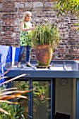 KARLA NEWELL GARDEN  BRIGHTON: KARLA PRUNES THE CAREX GRASS IN A TERRACOTTA CONTAINER ON TOP OF HER HOME OFFICE
