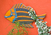 KARLA NEWELL GARDEN  BRIGHTON: SMALL TOWN GARDEN - ORANGE WALL WITH A CERAMIC FISH BOUGHT IN THE CARIBBEAN