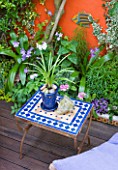 KARLA NEWELL GARDEN  BRIGHTON: SMALL TOWN GARDEN - ORANGE PAINTED WALL BESIDE WOODEN DECK WITH MOSAIC TABLE BOUGHT IN MOROCOO