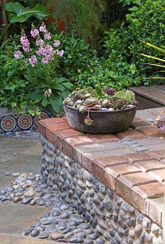 KARLA_NEWELL_GARDEN__BRIGHTON_SMALL_TOWN_GARDEN__WALL_MADE_OF_COBBLES_AND_BRICK_WITH_CONTAINER_SLATE