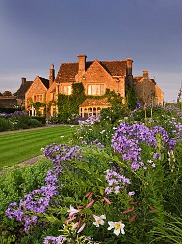 WHATLEY_MANOR__WILTSHIRE_VIEW_OF_THE_HOTEL_ACROSS_THE_LAWN_AND_HERBACEOUS_BORDER_AT_SUNSET_LILIUM_RE