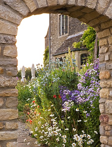 WHATLEY_MANOR__WILTSHIRE_HERBACEOUS_BORDER_SEEN_THROUGH_ARCHWAY_FROM_THE_KITCHEN_GARDEN