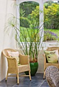 DESIGNER: CLARE MATTHEWS - HOUSEPLANT PROJECT - CONSERVATORY WITH WICKER CHAIRS AND GREEN GLAZED CONTAINER PLANTED WITH PAPYRUS