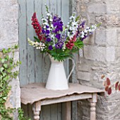 THE GARDEN AND PLANT COMPANY  HATHEROP CASTLE  CIRENCESTER  GLOUCESTERSHIRE: JUG WITH LUPINSBESIDE PALE BLUE DOOR