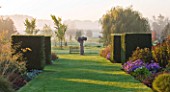 WATERPERRY GARDENS  OXFORDSHIRE: VIEW ALONG BORDER TO SCULPTURE WITH COUNTRYSIDE BEYOND AT DAWN