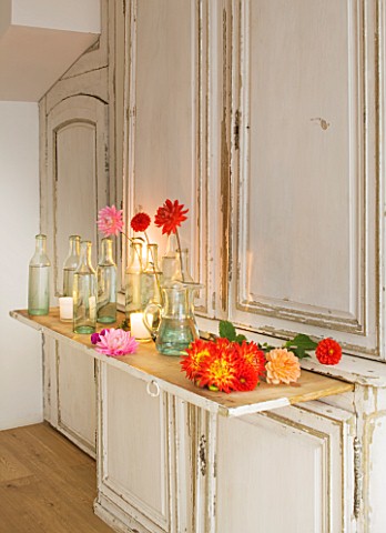 JACKY_HOBBS_HOUSE__LONDON_BRIGHTLY_COLOURED_CUT_DAHLIA_BLOOMS_IN_BOTTLES_ON_VINTAGE_FRENCH_DRESSER